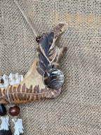 Kauriin leukaluusta, saniaisista, sulista, luusta tehty seinäkoriste. Lähikuva lehtokurpan sulkien yksityiskohdista.