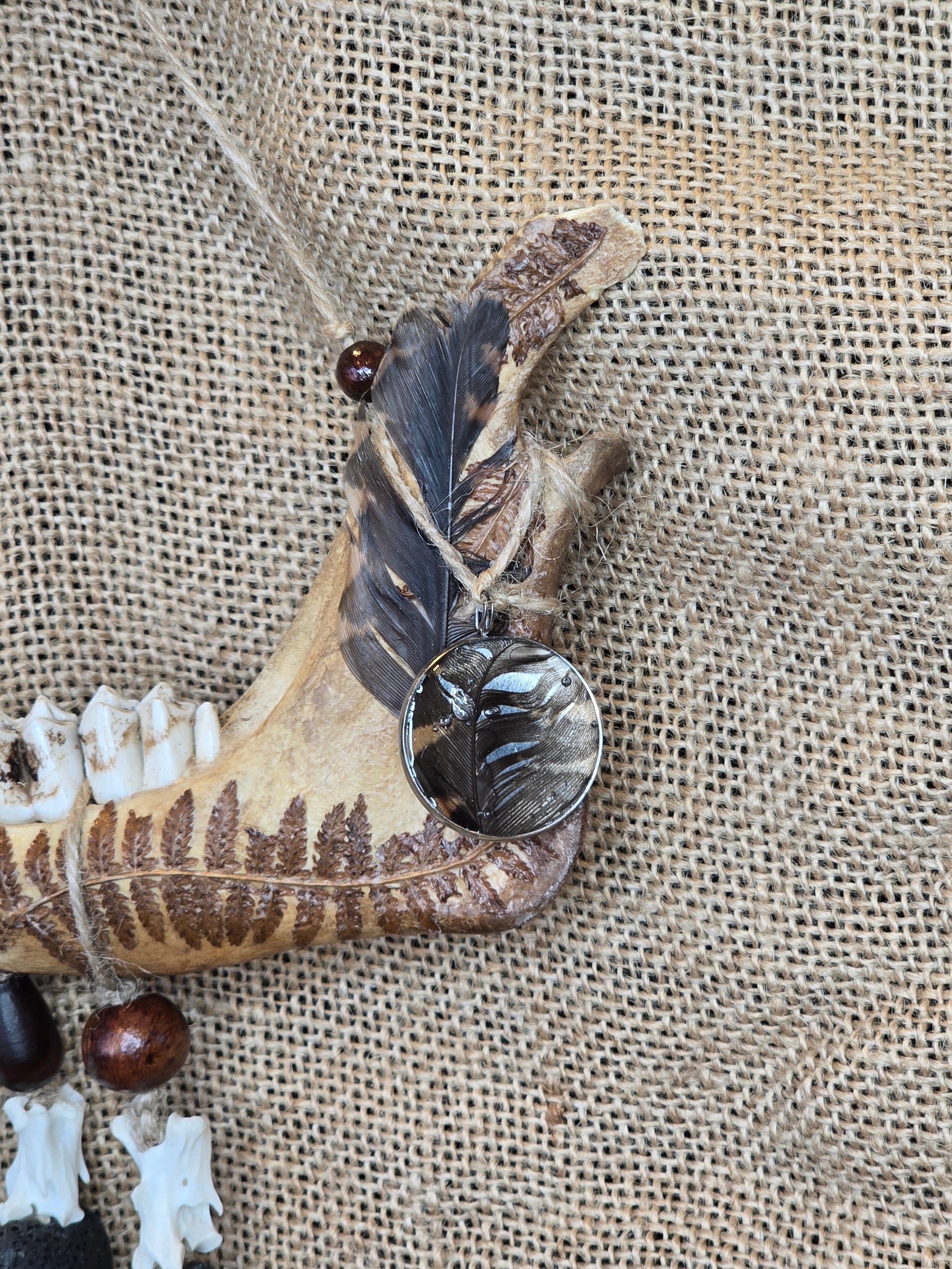 Kauriin leukaluusta, saniaisista, sulista, luusta tehty seinäkoriste. Lähikuva lehtokurpan sulkien yksityiskohdista.