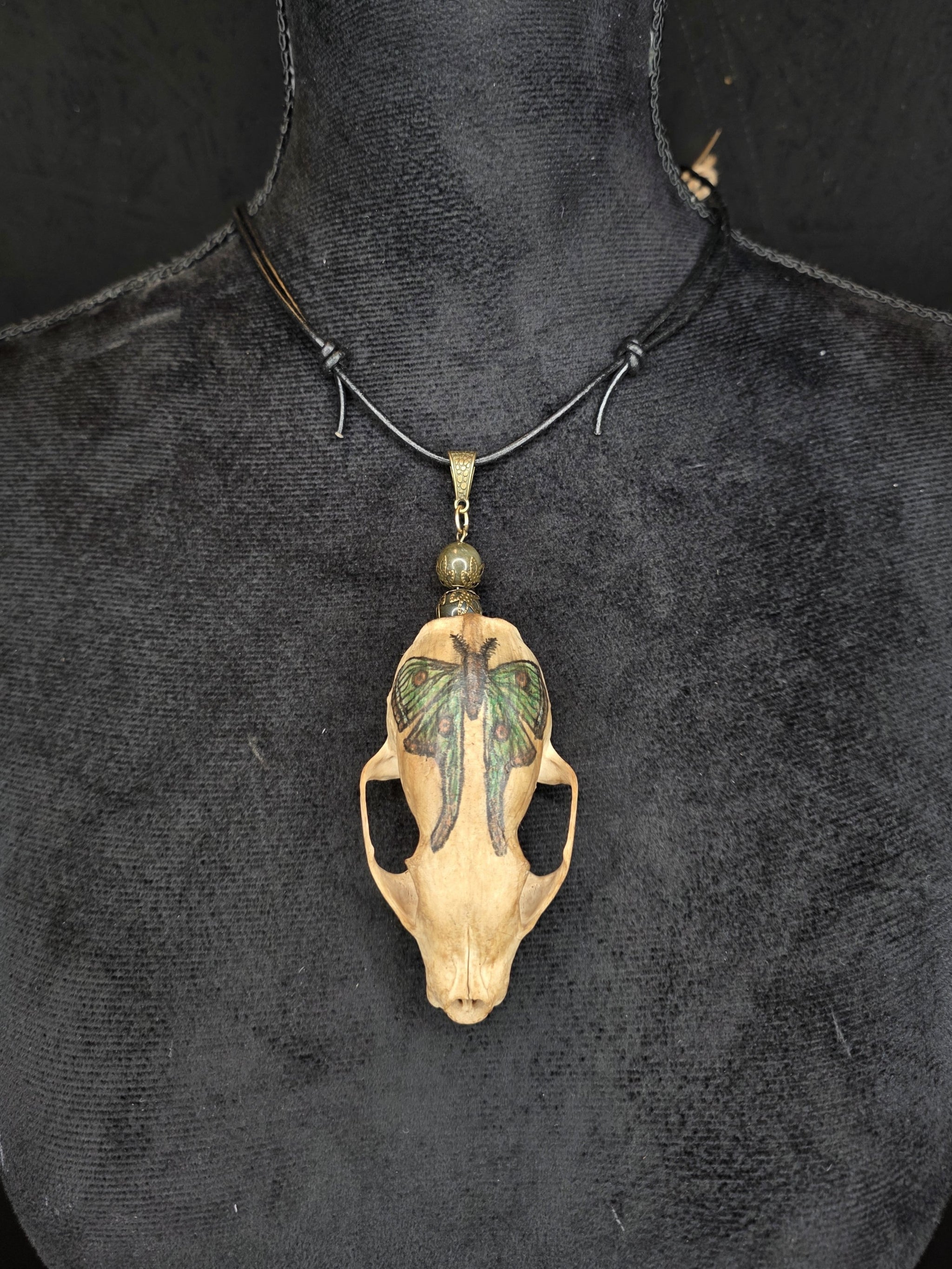 Minkinkallosta valmistettu näyttävä amuletti, jossa labradoriittihelmiä. Kallo on koristeltu perhoskuviolla. 