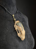 Minkinkallosta valmistettu näyttävä amuletti, jossa labradoriittihelmiä. Kallo on koristeltu perhoskuviolla. Amuletti sivulta.