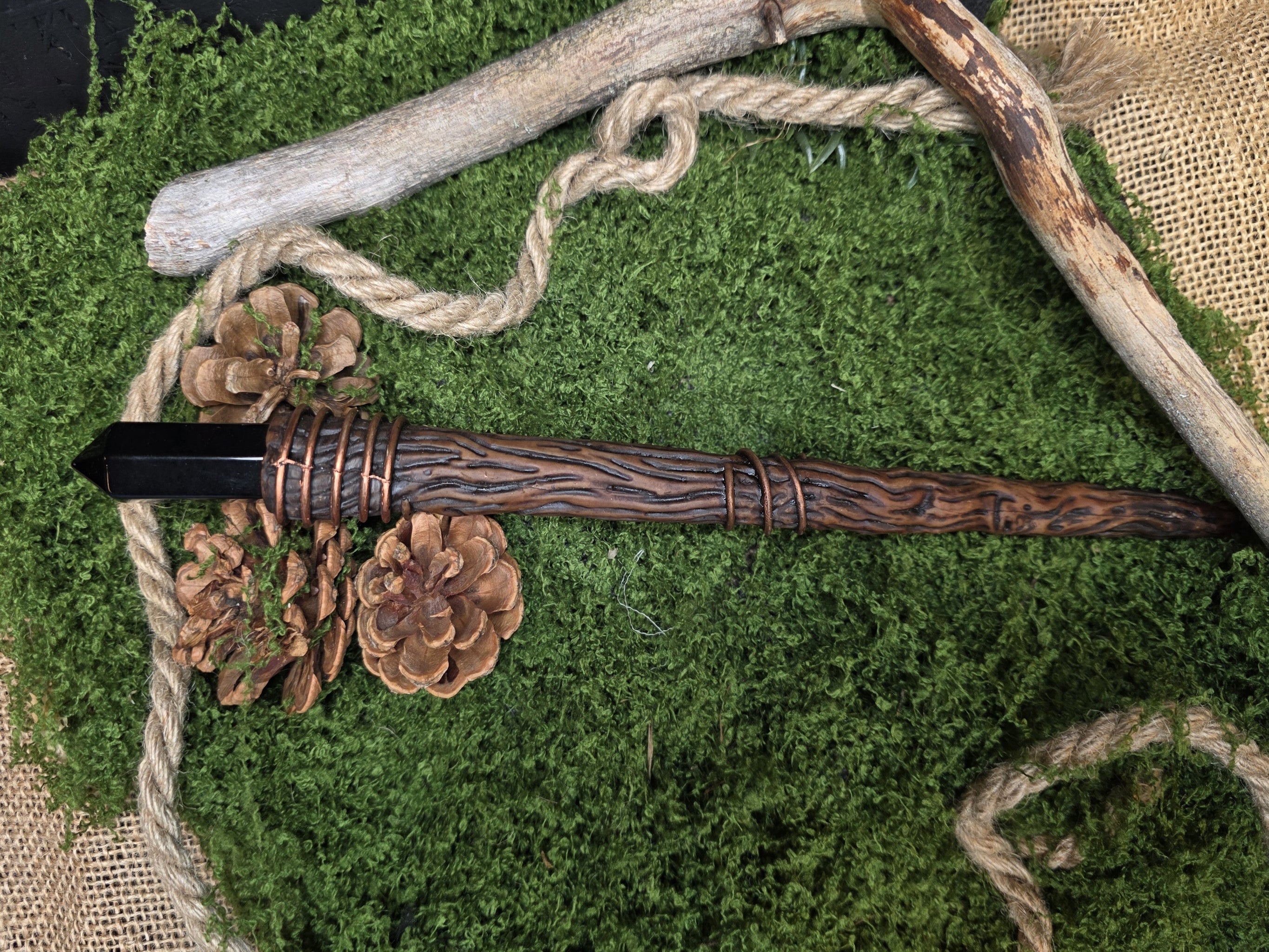 29 cm pitkä sauva, jonka päässä on aito obsidiaani kivi. Sauvan materiaali on puukuvioitu epoksihartsi.