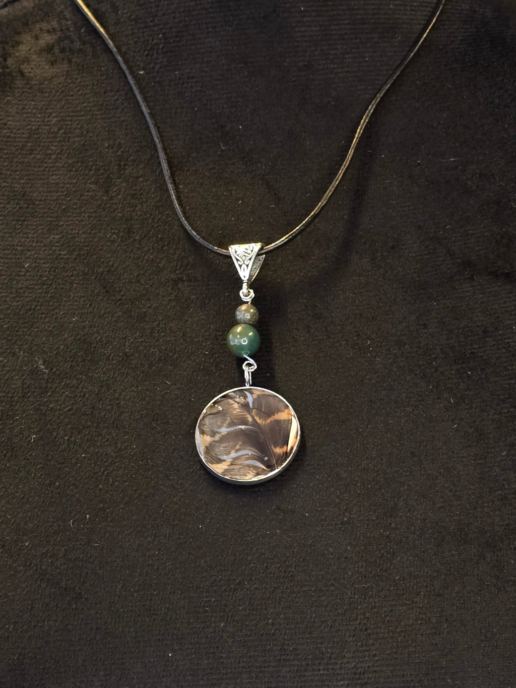 Metsän Kajo niminen amuletti, jossa on hartsi amuletin sisällä lehtokurpan sulka, ja sammalakaatti ja pyriittihelmet.