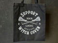 Support Your Local Witch Coven tekstillä varustettu musta kangaskassi.