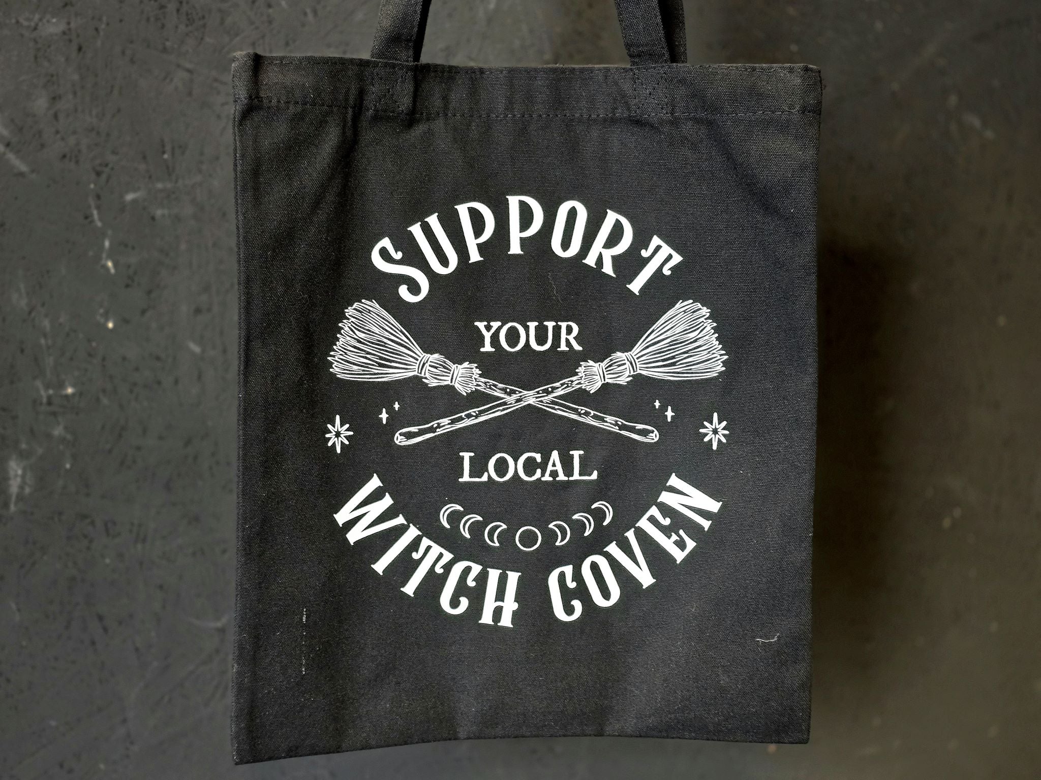 Support Your Local Witch Coven tekstillä varustettu musta kangaskassi.