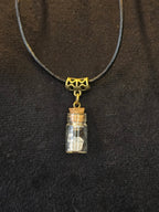 Lasipulloriipus, jonka sisällä vuorikristalli ja variksen kynsi. Valo ja Varjo.