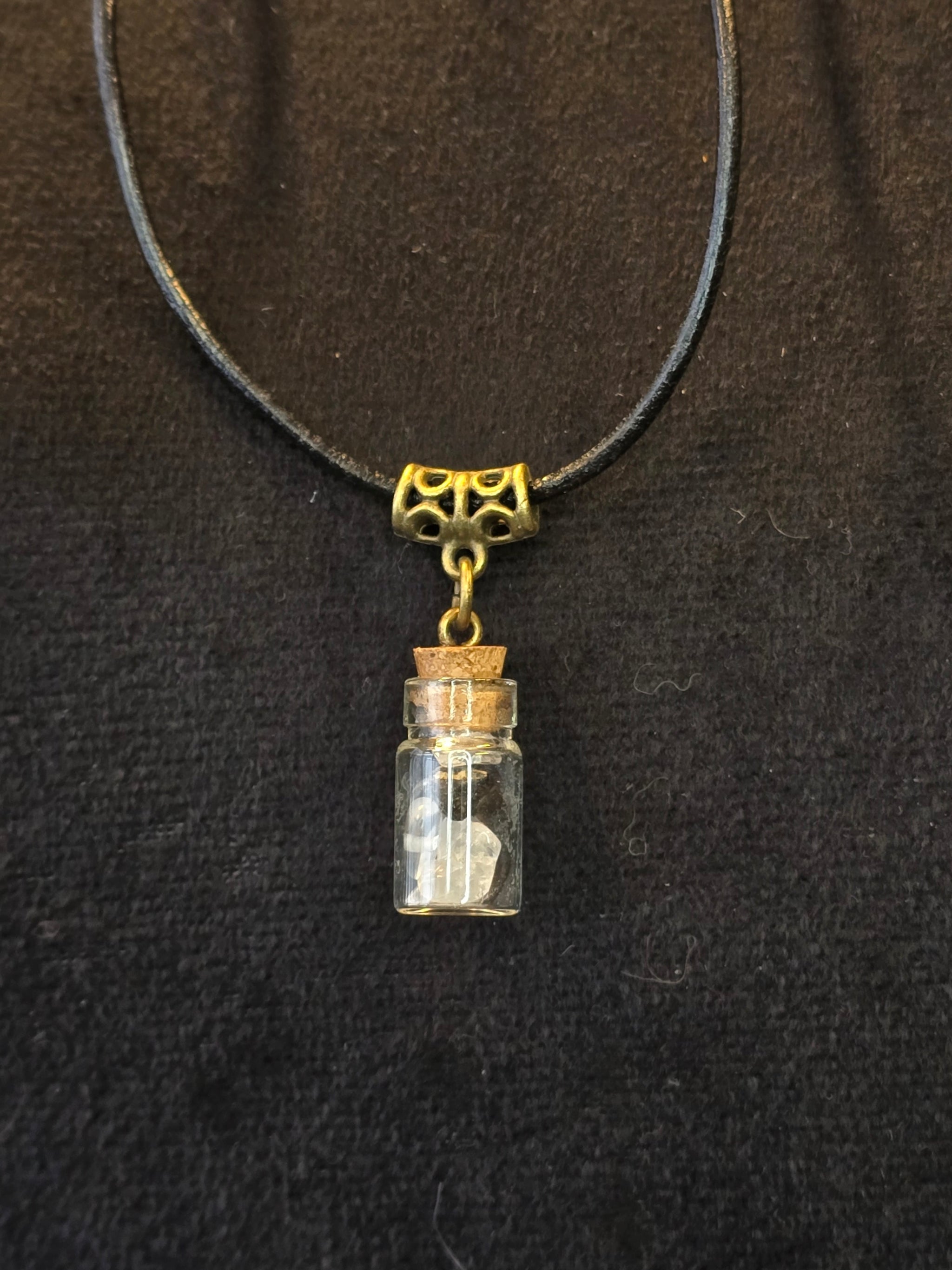 Lasipulloriipus, jonka sisällä vuorikristalli ja variksen kynsi. Valo ja Varjo.