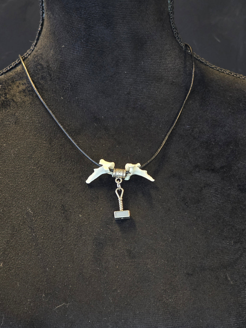 Kaulakoru, jossa thorin vasara symboli ja variksen nikamat. 