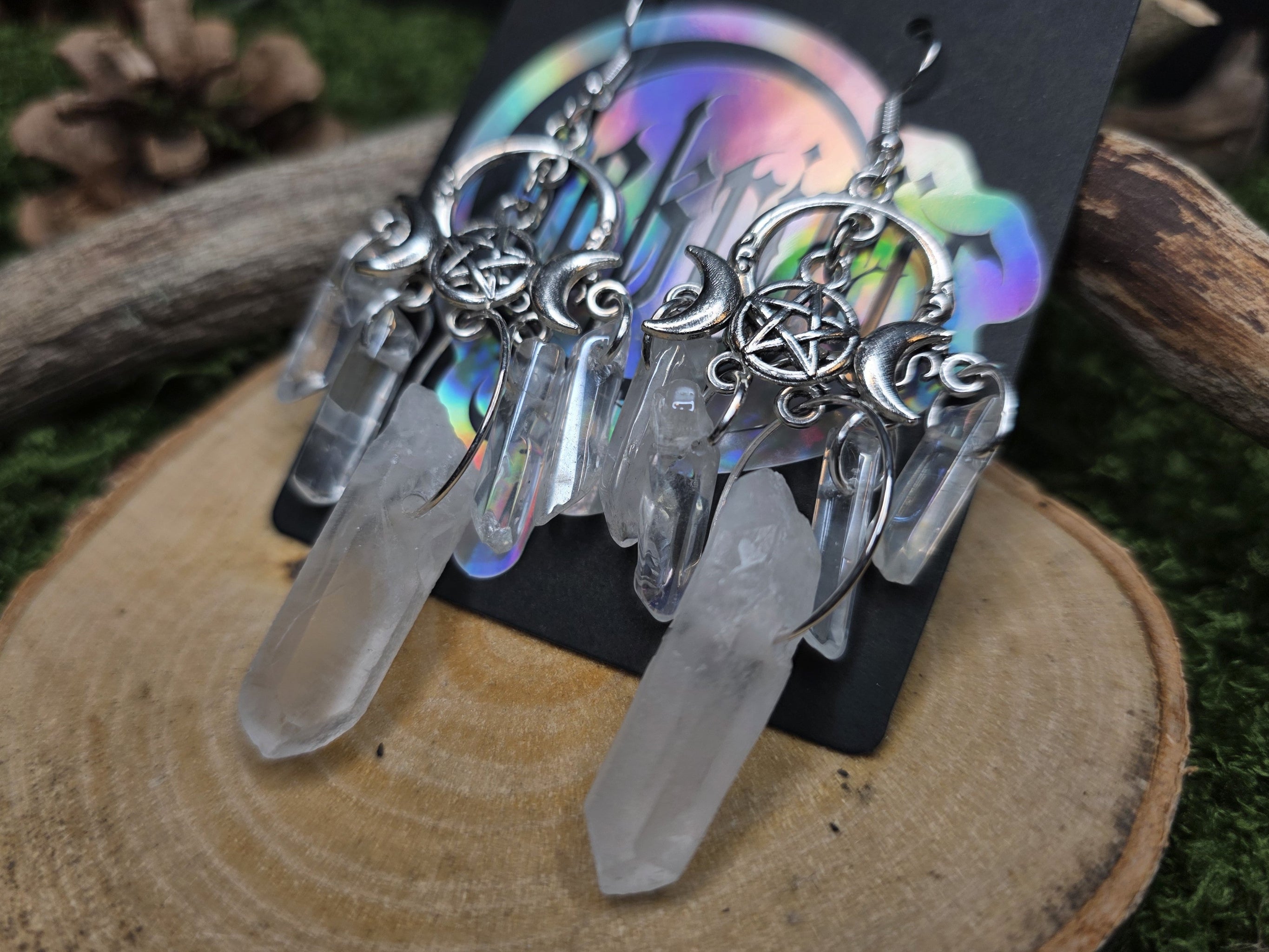 Näyttävät suuret vuorikristallista ja aurakvartsista valmistetut korvakorut, joissa triple moon somiste. Lähikuva.