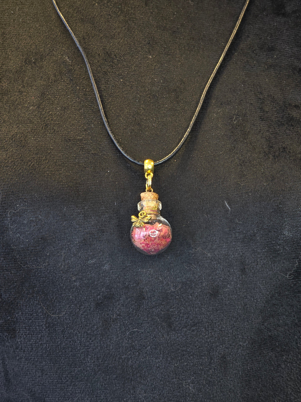 Kaulakoru, jossa lasipulloriipuksen sisällä ruusunterälehtiä ja rodoniittikivi, somisteena pieni yöperhonen riipus. 