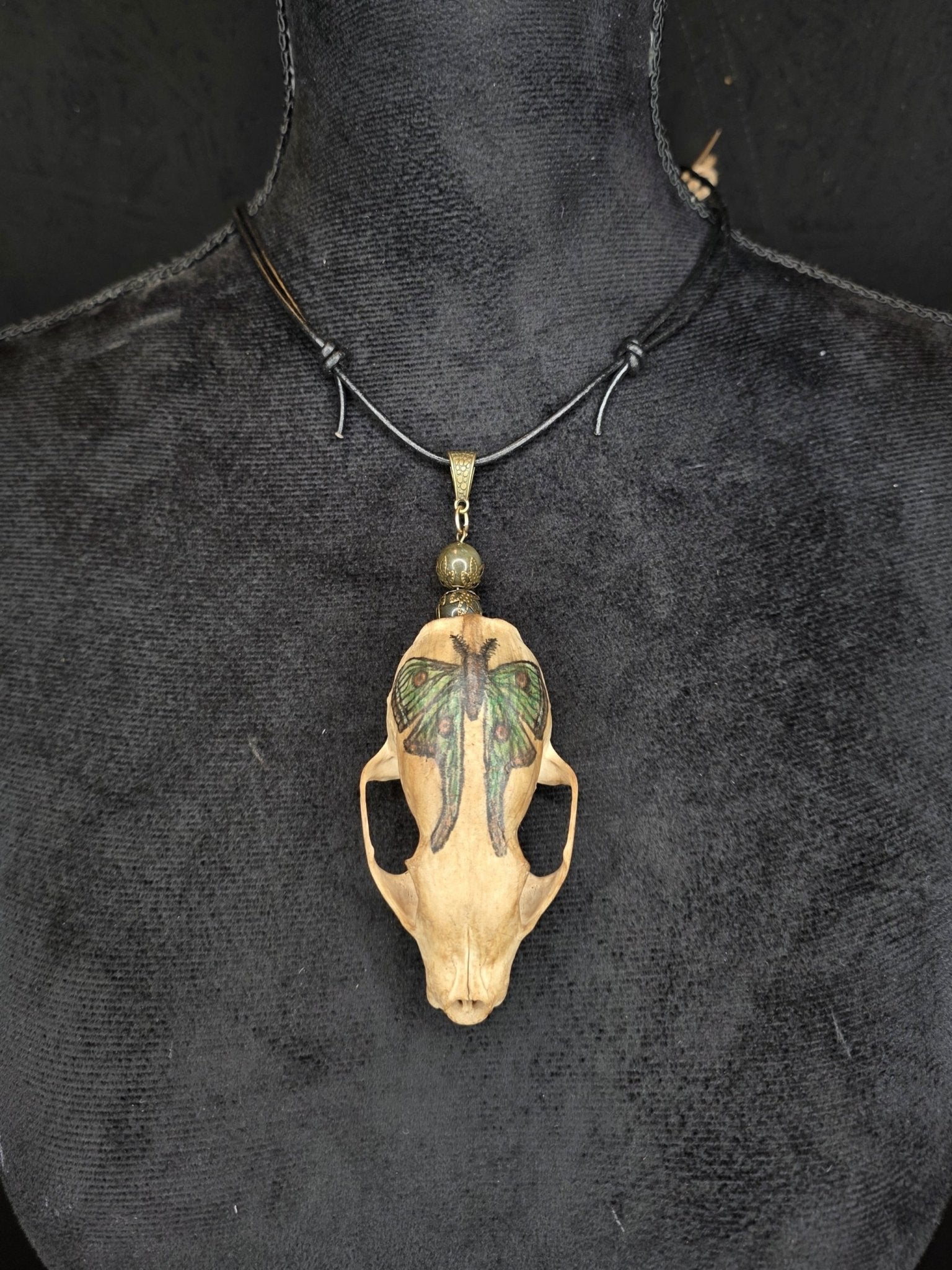 Minkinkallosta valmistettu näyttävä amuletti, jossa labradoriittihelmiä. Kallo on koristeltu perhoskuviolla. 