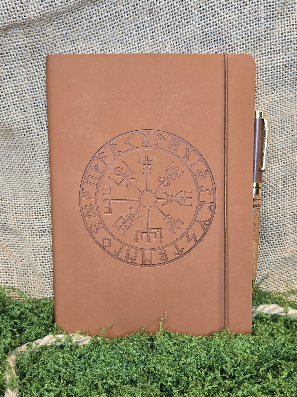 Ruskea muistikirja vegvisir symbolilla ja kynällä edestä.