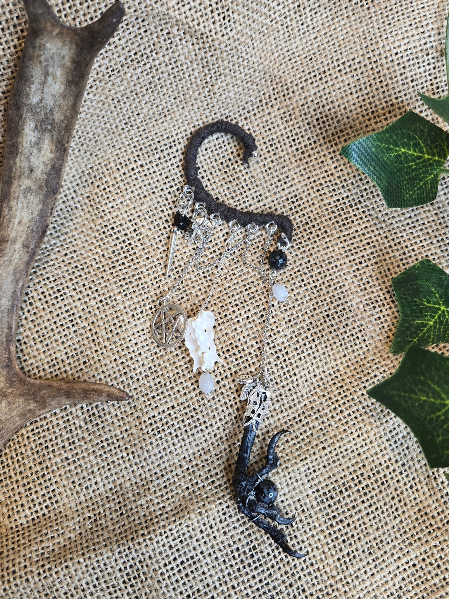 Tumma korvakääty, jossa pentagram riipus, rotanluu, kuukivihelmet, naakan koipi ja astrofyllittihelmet. 