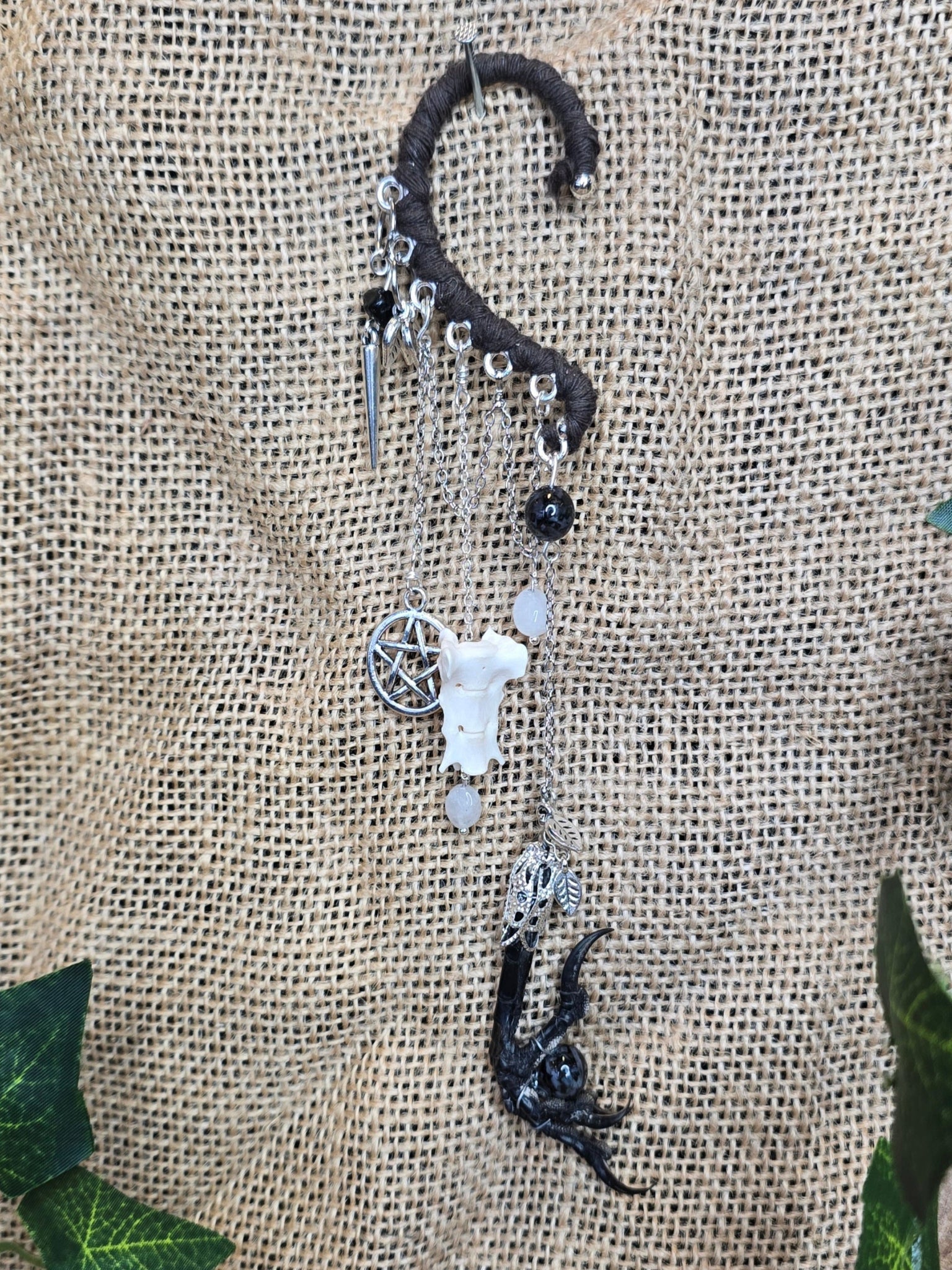 Tumma korvakääty, jossa pentagram riipus, rotanluu, kuukivihelmet, naakan koipi ja astrofyllittihelmet. 