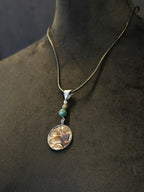 Metsän Kajo niminen amuletti, jossa on hartsi amuletin sisällä lehtokurpan sulka, ja sammalakaatti ja pyriittihelmet.