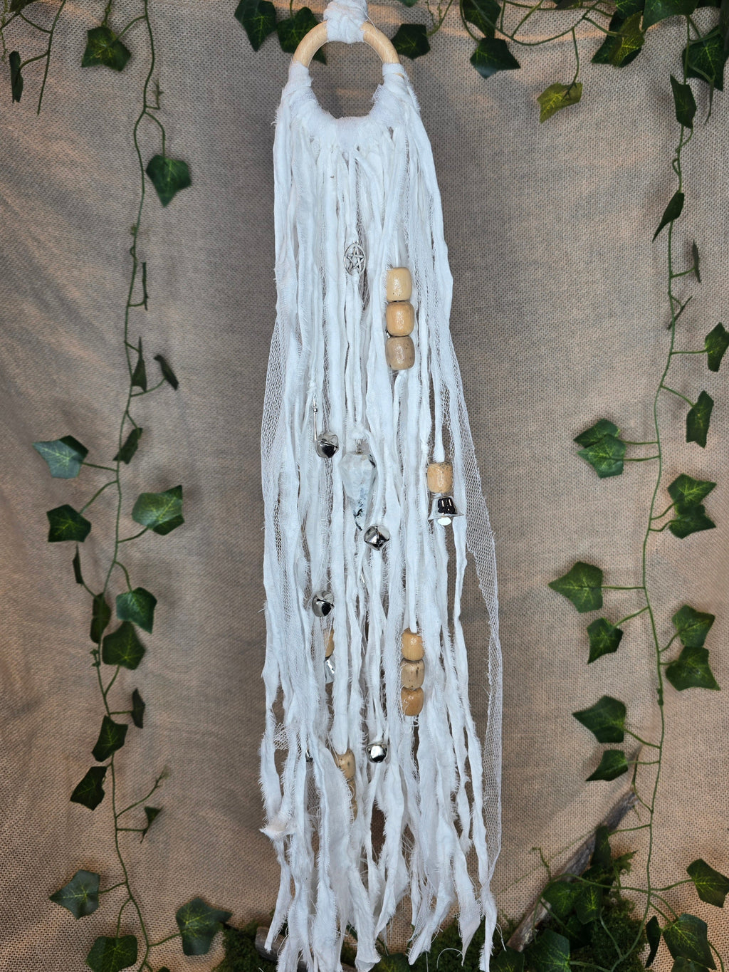 Valkoinen noitakello, jossa puuhelmiä, hopeisia kelloja, pentagram riipus ja kuukivi.