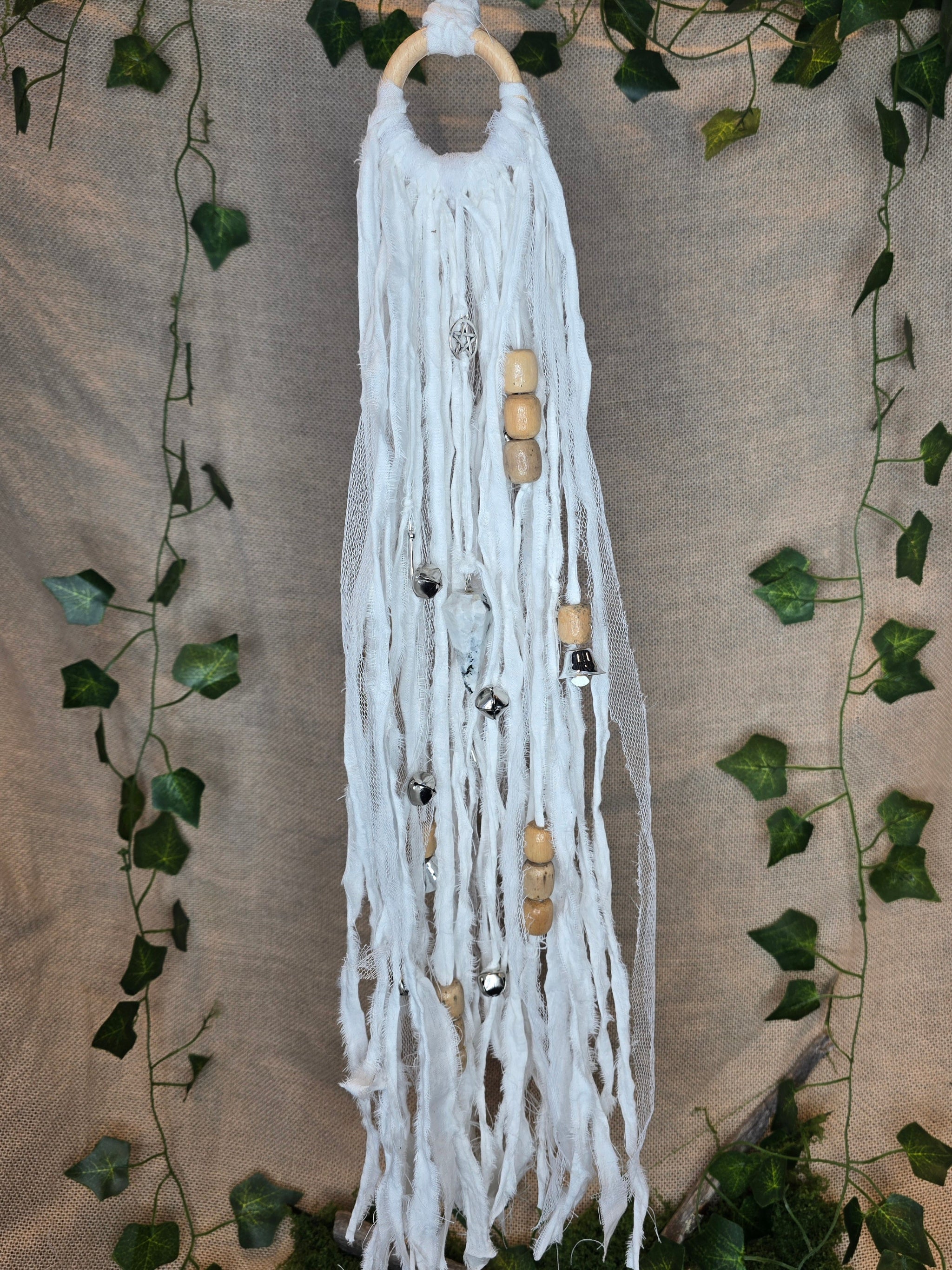 Valkoinen noitakello, jossa puuhelmiä, hopeisia kelloja, pentagram riipus ja kuukivi.