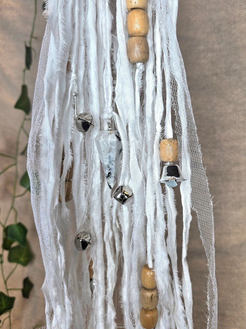 Valkoinen noitakello, jossa puuhelmiä, hopeisia kelloja, pentagram riipus ja kuukivi.