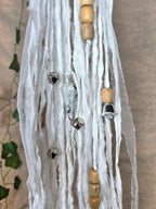 Valkoinen noitakello, jossa puuhelmiä, hopeisia kelloja, pentagram riipus ja kuukivi.