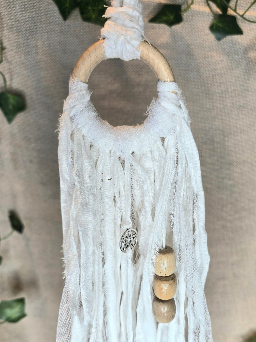 Valkoinen noitakello, jossa puuhelmiä, hopeisia kelloja, pentagram riipus ja kuukivi.