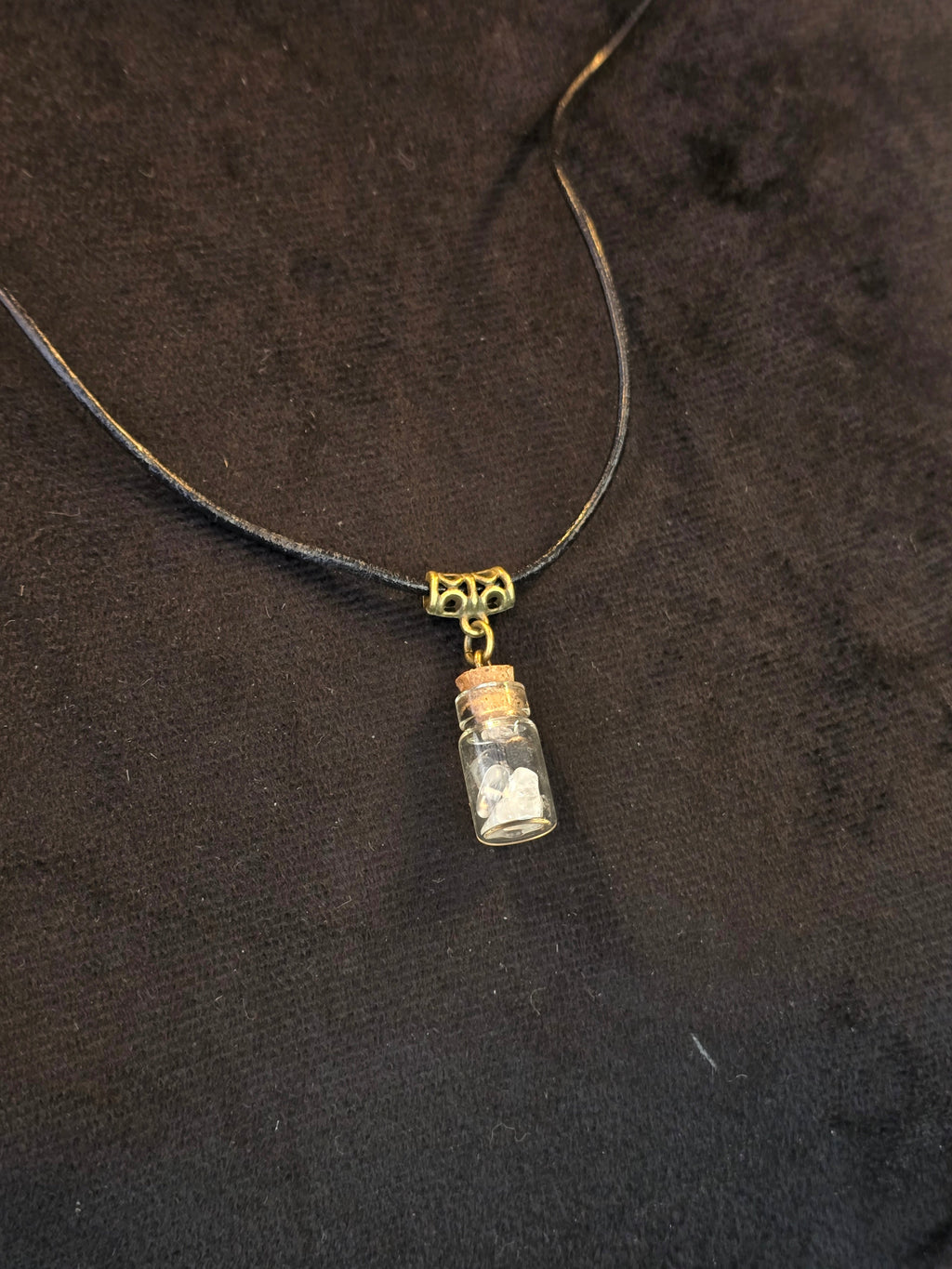 Lasipulloriipus, jonka sisällä vuorikristalli ja variksen kynsi. Valo ja Varjo.