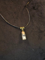 Lasipulloriipus, jonka sisällä vuorikristalli ja variksen kynsi. Valo ja Varjo.