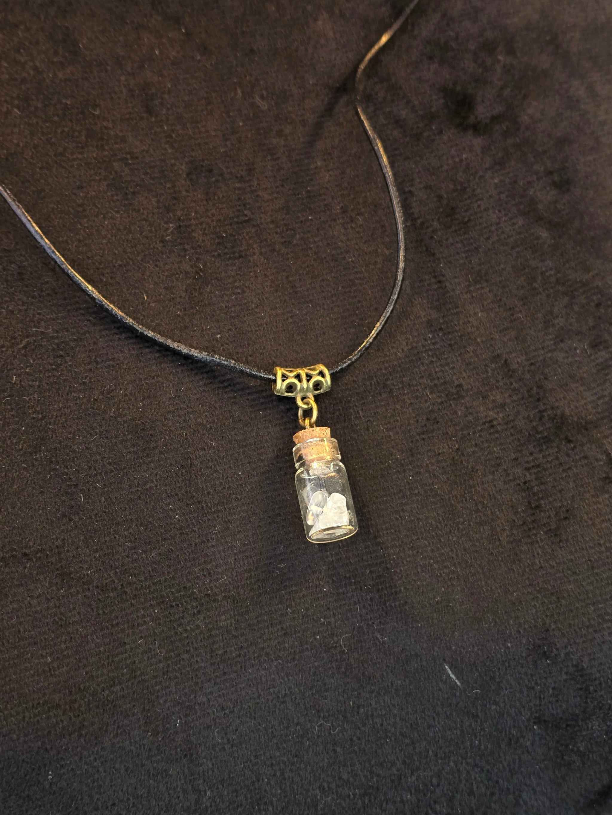 Lasipulloriipus, jonka sisällä vuorikristalli ja variksen kynsi. Valo ja Varjo.