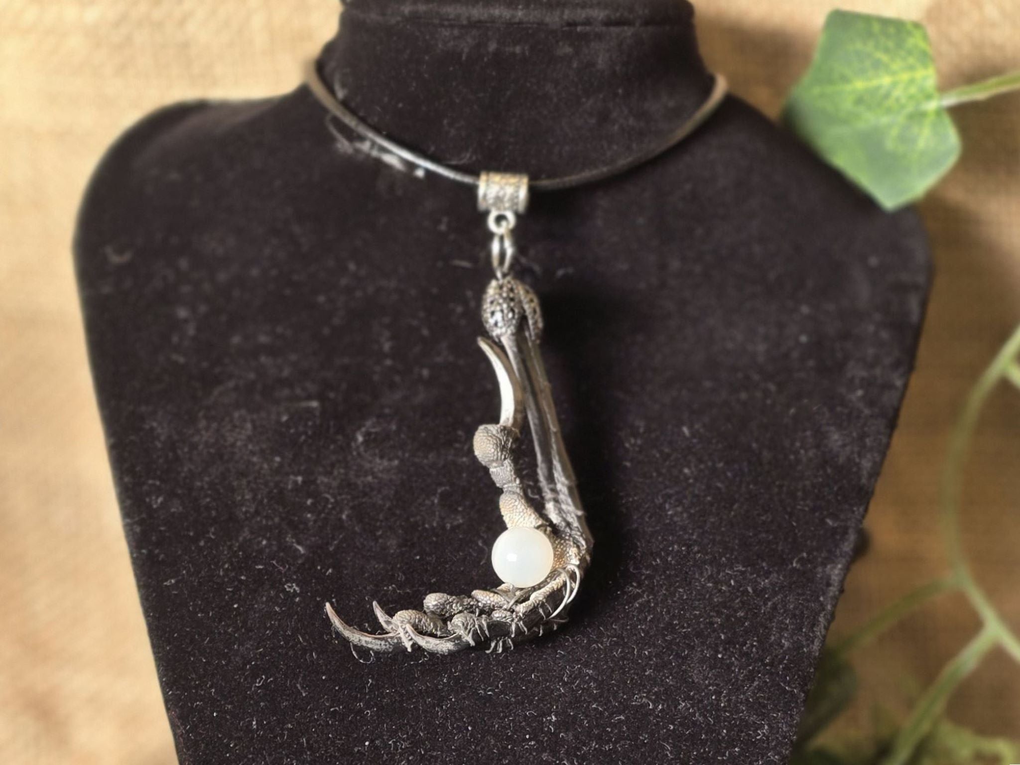 Varis ja seleniitti kaulakoru, jossa variksen jalka pitelee seleniitti helmeä. Kuunjuurella valmistama, Inked Mystiqs noitakaupasta. 