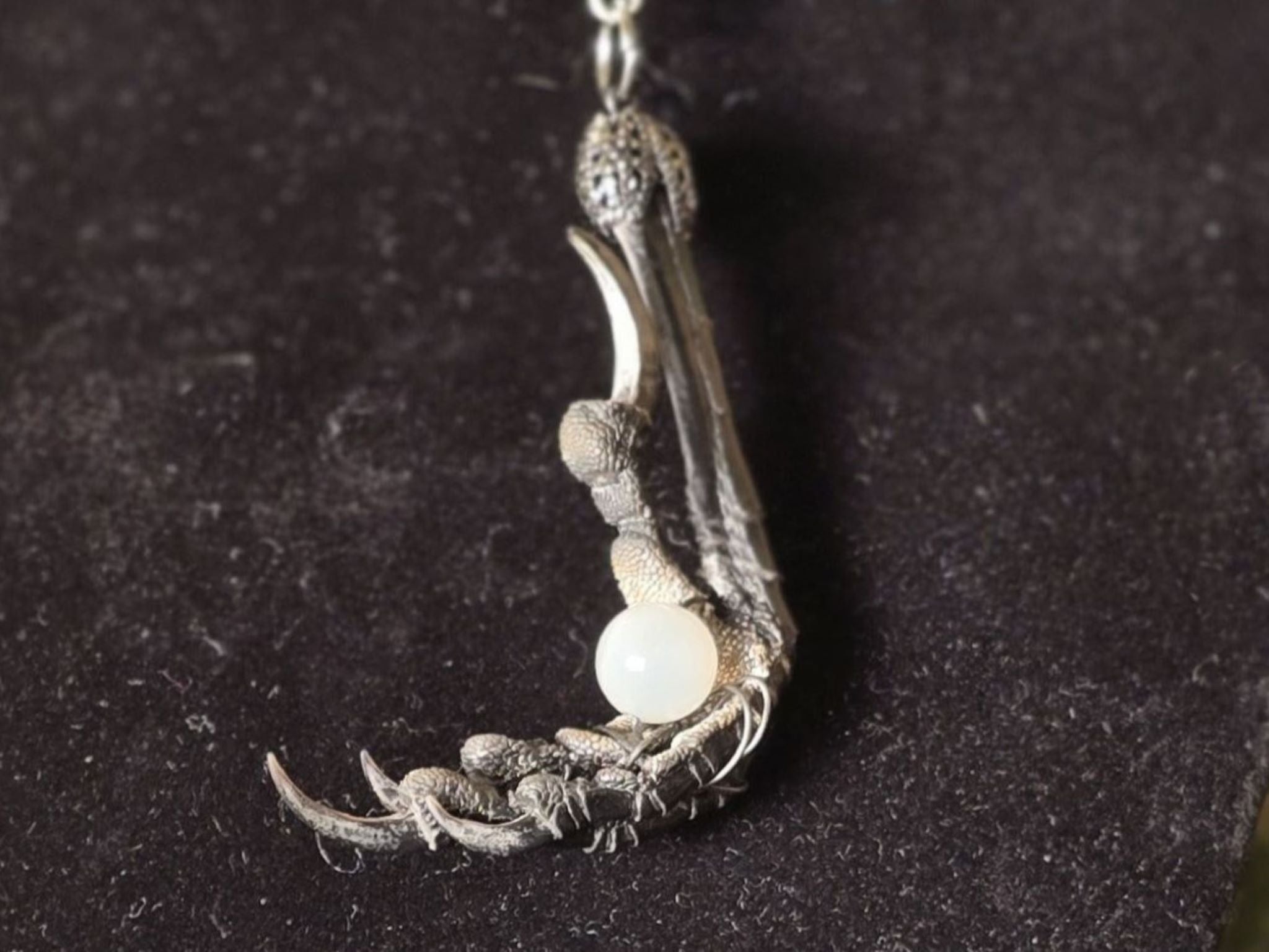 Varis ja seleniitti kaulakoru, jossa variksen jalka pitelee seleniitti helmeä. Kuunjuurella valmistama, Inked Mystiqs noitakaupasta. Lähikuva.