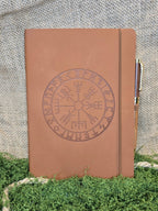 Ruskea muistikirja vegvisir symbolilla ja kynällä edestä.